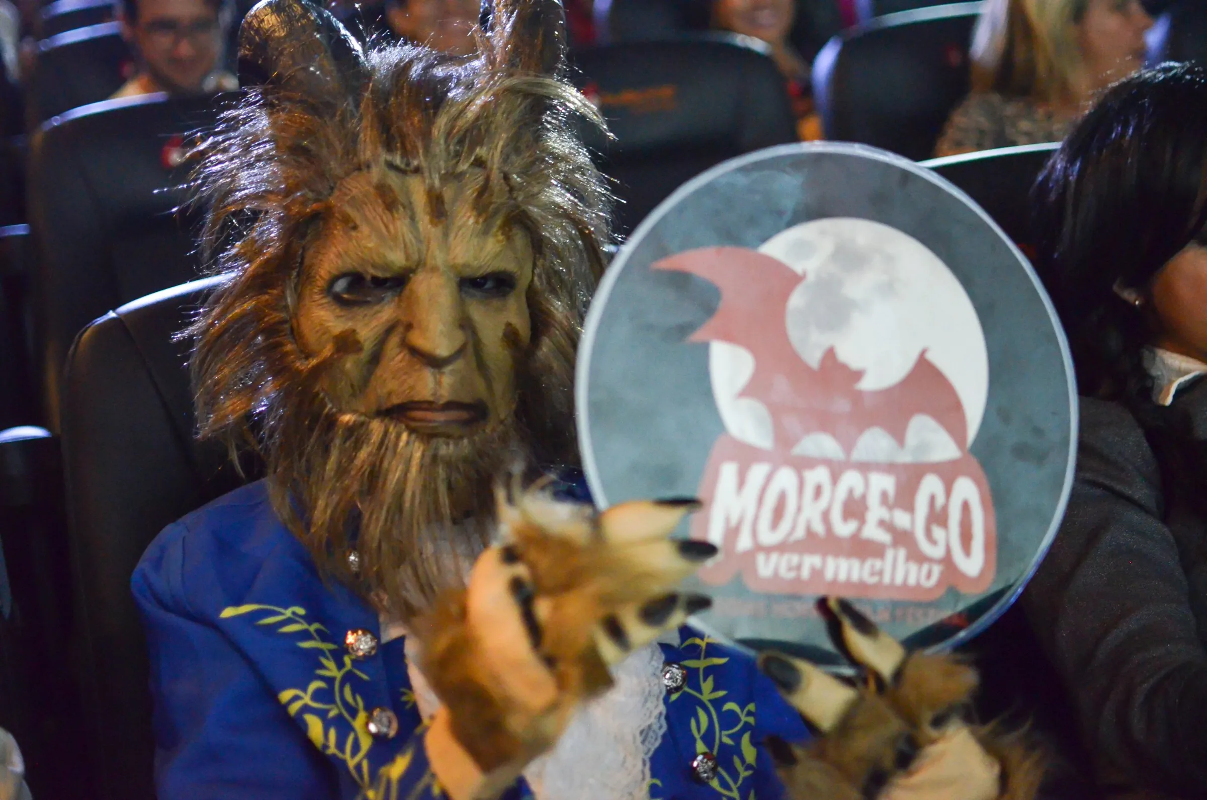 Cosplay da Fera, com máscara peluda, segurando uma placa do Morce-GO na plateia.