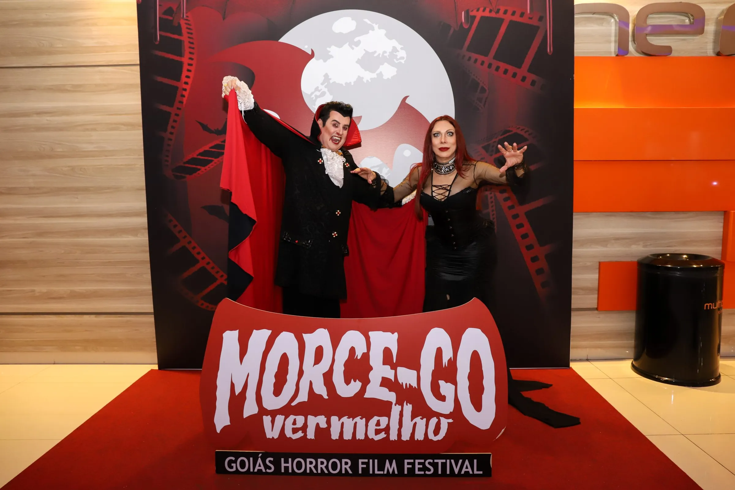 O vampiro Morcegão e uma convidada de preto posam diante do painel do Morce-GO.