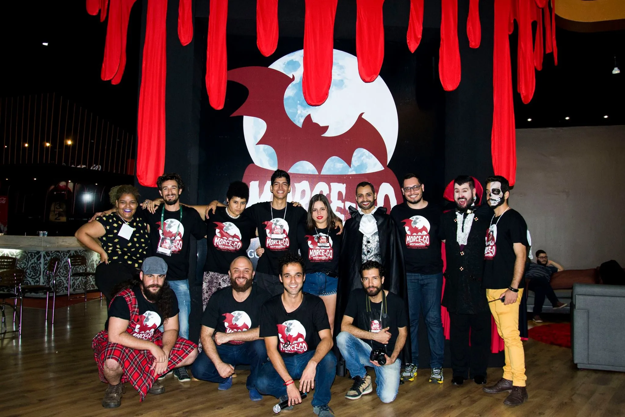 Equipe do festival reunida diante do palco com cortinas de sangue.