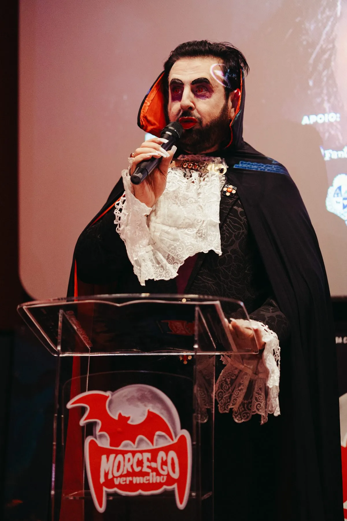 Apresentador vestido de vampiro discursa no púlpito do festival